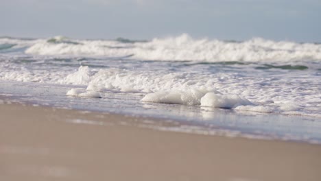 brechende wellen spülen weißen schaum am sandstrand von sylt in deutschland