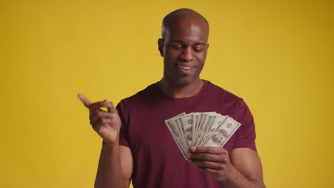 studio shot of excited mature man celebrating winning cash prize counting and throwing handful of 100 dollar bills in the air