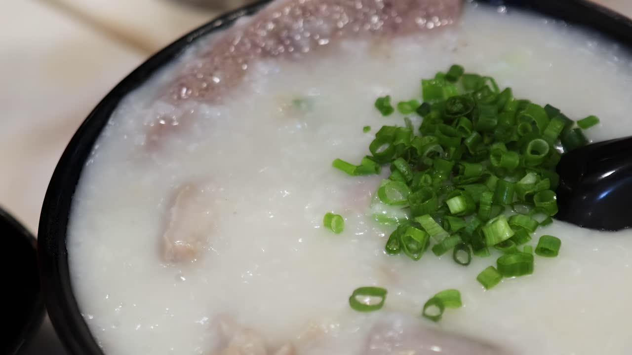 A close-up view of creamy porridge garnished with vibrant green onions, served in a black bowl.