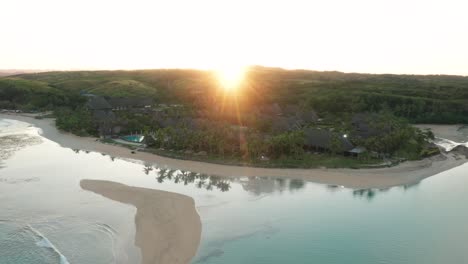 Bright-sun-shines-over-hill-into-tropical-bay-on-shore-of-mainland-Fiji,-aerial