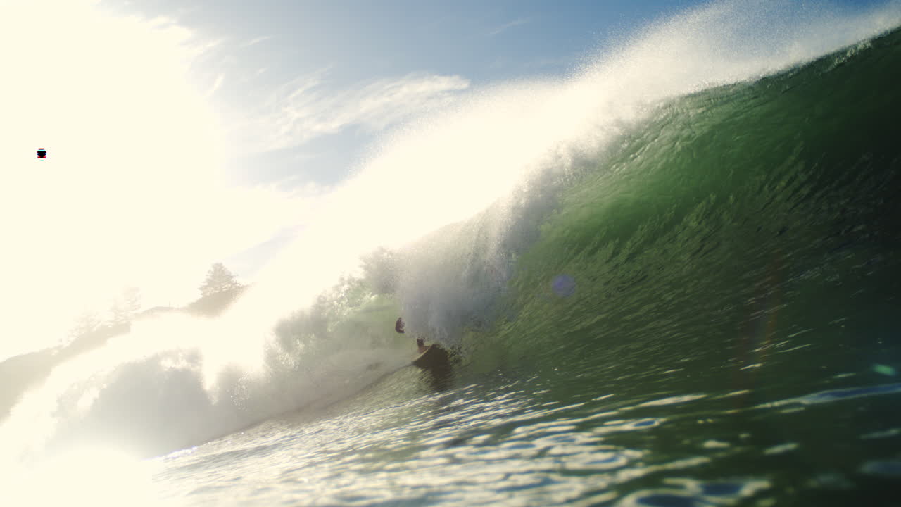 Super slow motion surfer emerges from barreling shorebreak at sunrise with glistening water spray