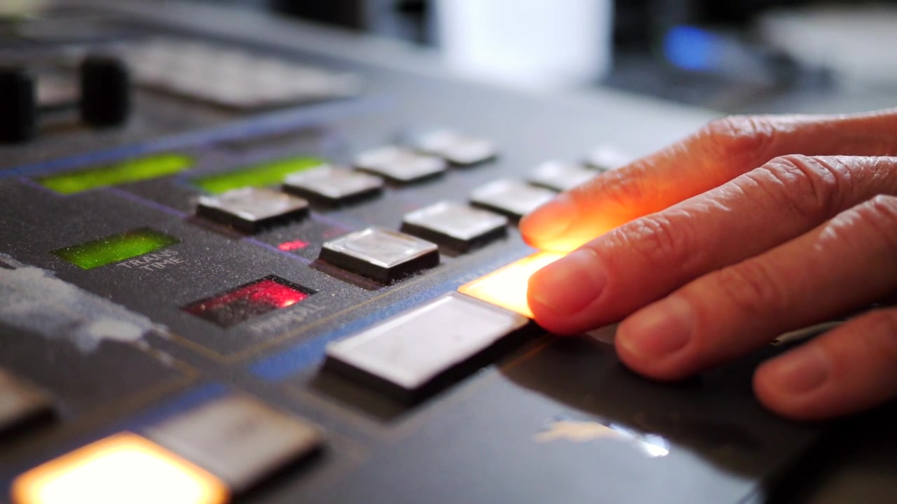 Primo piano di un operatore di studio televisivo che lavora su una console di controllo professionale per trasmissioni durante una produzione TV in diretta