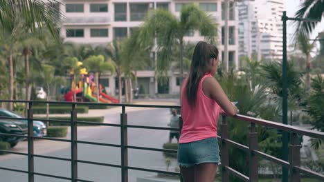 young-tanned-lady-with-long-hair-leans-on-balcony-fence