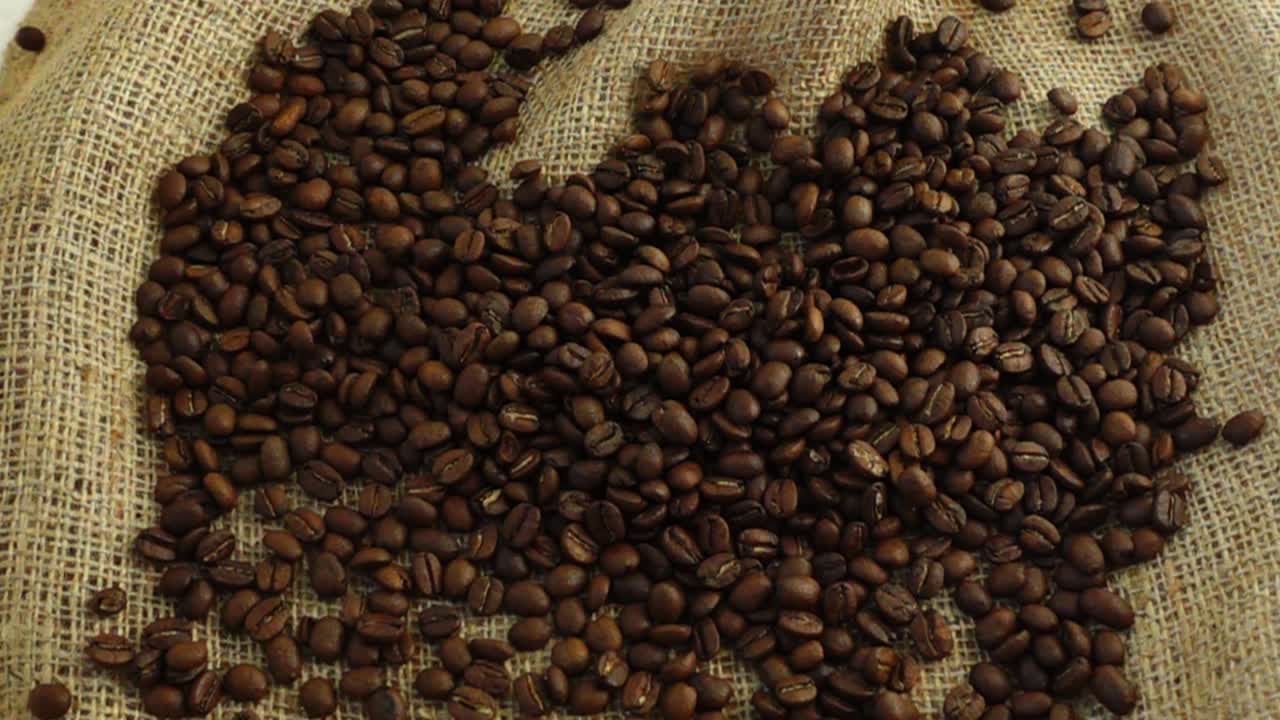 Chicchi di caffè cadono su tela di iuta al rallentatore.