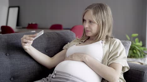 smiling pregnant woman showing belly during video call