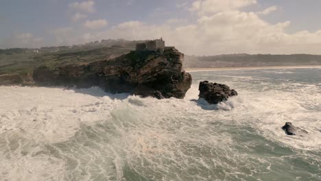 Riesige-Wellen-Brechen-Gegen-Die-Klippen-Der-Festung-Sao-Miguel-Arcanjo-In-Nazare,-Portugal