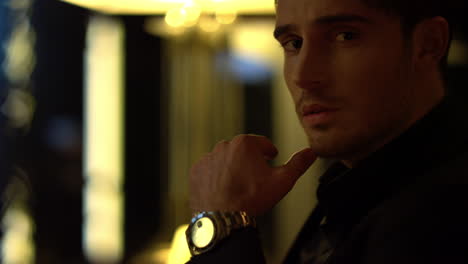stylish man looking camera dark background. beautiful guy touching chin indoors.