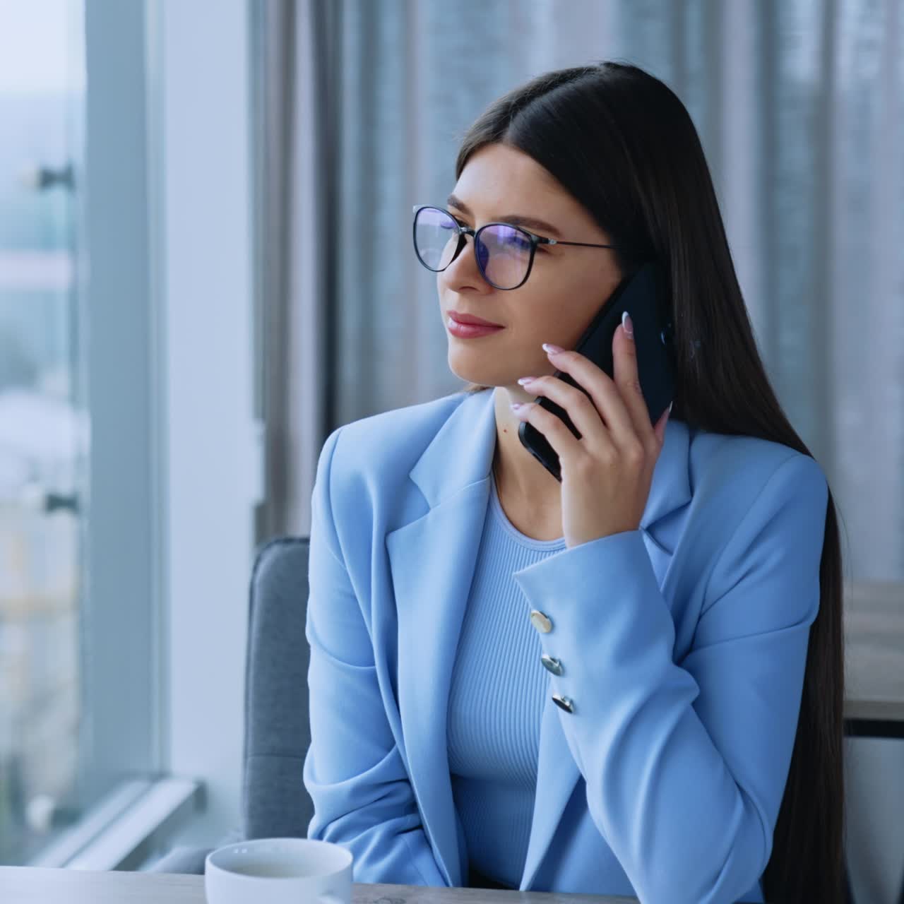 Bellissima donna bruna seduta alla scrivania in ufficio, impegnata in una conversazione telefonica. Donna con gli occhiali che parla con i clienti, discutendo e risolvendo problemi. Primo piano