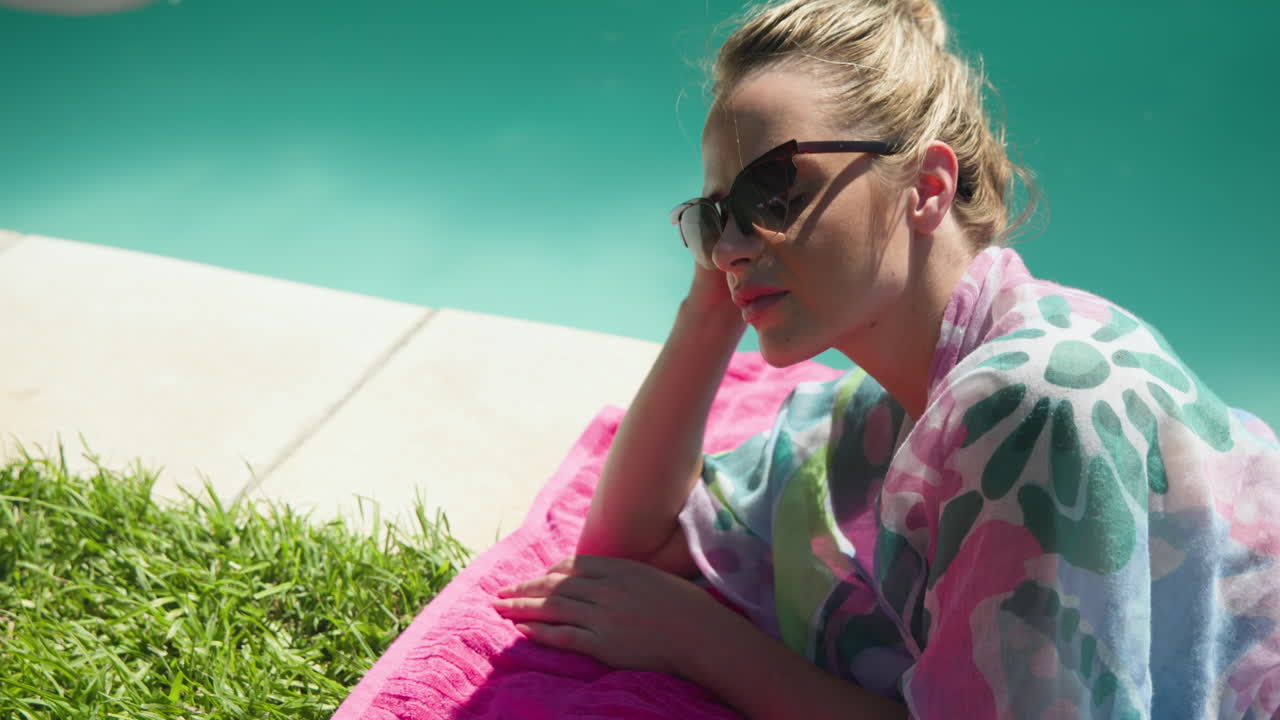 Relaxing by pool, woman in sunglasses sunbathing on pink towel, enjoying leisure, copy space