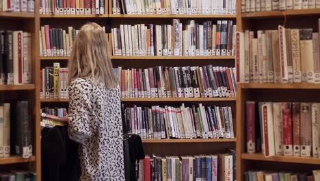 una joven caminando entre estanterías en la biblioteca, con una plataforma rodante con libros por todas partes