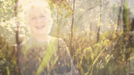 Animación-De-Puntos-De-Luz-Y-árboles-Sobre-Una-Mujer-Caucásica-Mayor-Sonriente-En-El-Jardín