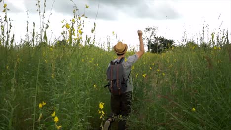 happy and joyful male tourist backpacker with hat and bag excitedly walking and jumping on the countryside grassland