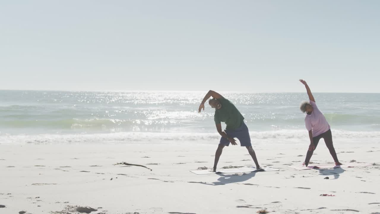 행복한 노인 아프리카계 미국인 커플이 요가를 하고 해변에서 스트레칭을 하고, 스로우 모션으로 공간을 복사합니다.