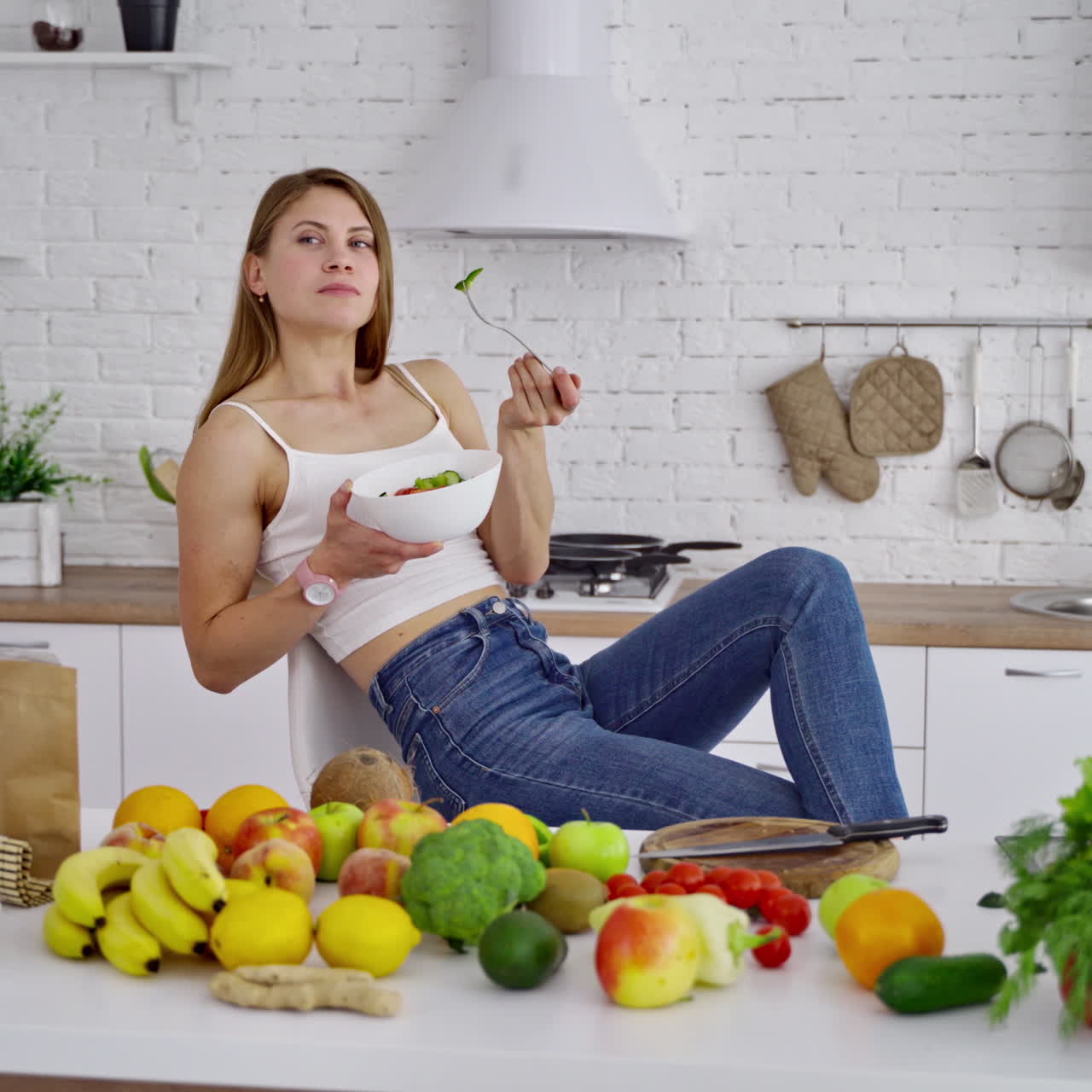 Beautiful woman in the light kitchen. Young female vegetarian enjoys eating fresh food. Organic fruit and vegetables laying on the table. Dieting concept.