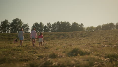 familia caminando juntos por la colina de la granja en un día soleado con el perro, la vista trasera muestra a dos mujeres y un niño pequeño en el medio sosteniendo la correa del perro, disfrutando de la naturaleza y el tranquilo campo