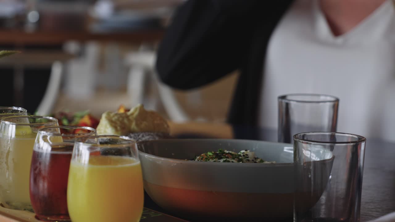 Filmato 4K di un tavolo da brunch con sana insalata Caesar e succhi freschi tra cui succo d'arancia e succo di mela, che mostra bevande colorate e una presentazione culinaria gourmet.