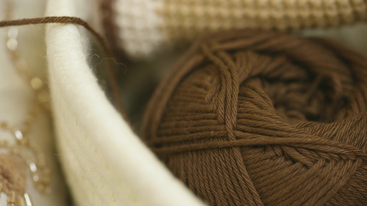 A very close-up shot that highlights a skein of brown-toned yarn with a soft texture and defined weave, housed in a light-colored fabric container