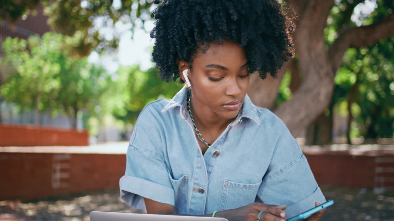 Teenager headphones turning music at smartphone sitting park with laptop closeup