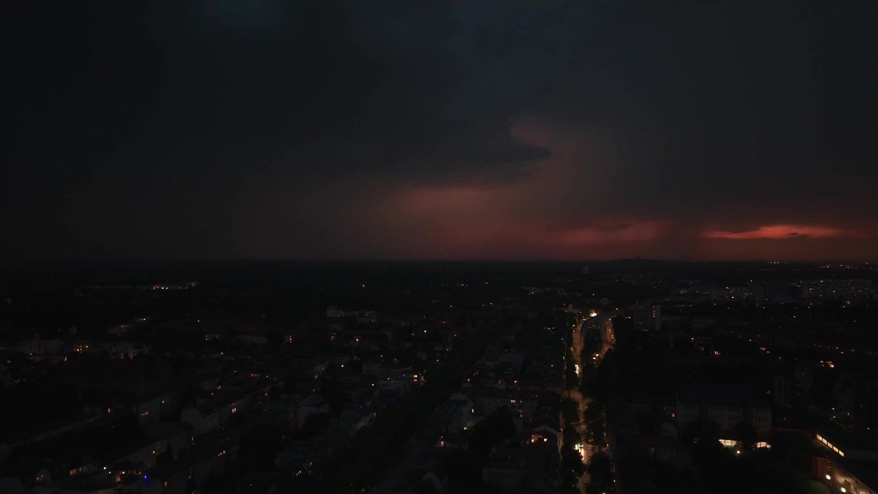 Blesky blikající nad městem v noci, osvětlující mraky a panorama s auty jedoucími po ulici během bouřky. Úžasný letecký pohled dronem, panoramatický záběr shora.