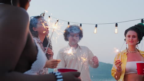 cheerful people dancing with sparklers at lake party