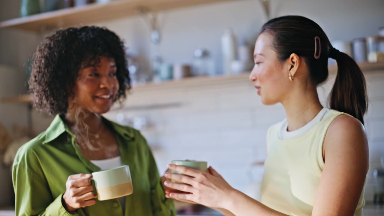Multiracial friends chatting coffee home kitchen. Women holding morning mugs