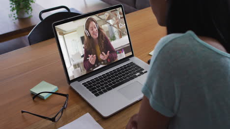 biracial businesswoman sitting at desk using laptop having video call with female colleague