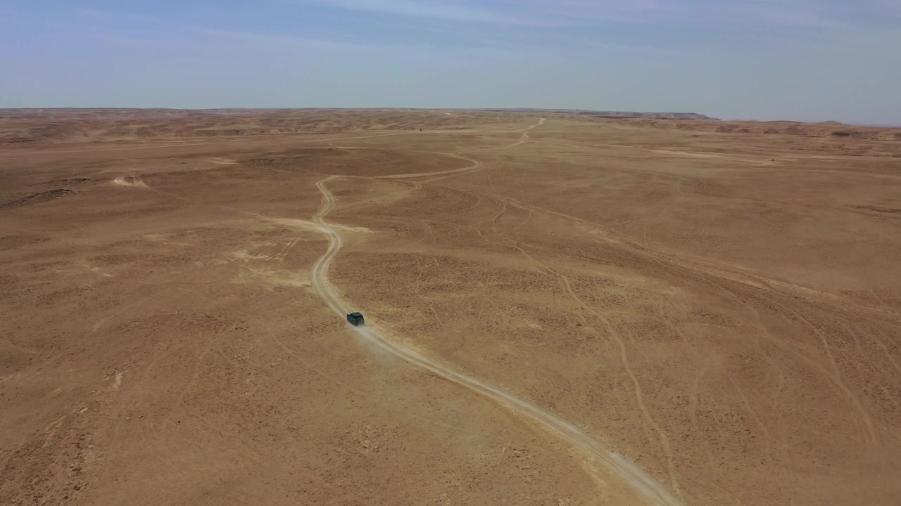Ripresa aerea con drone di un'auto che percorre una pista sterrata isolata attraverso l'ampio e aspro altopiano desertico vicino a Edge of the World, Arabia Saudita, che mostra viaggi remoti e avventura.