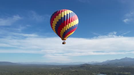 Vista-Aérea-Del-Paracaídas-De-Globo-De-Aire-Caliente-Multicolor-Que-Vuela-Sobre-El-Paisaje-Y-El-Lago-En-Un-Día-Soleado