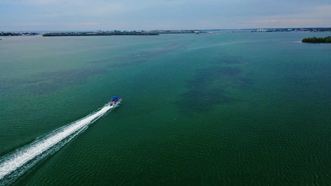 A lone boat cuts a white trail across the calm green expanse of Lemon Bay as it moves toward the Manasota Key coastline on Florida’s quiet Gulf Coast