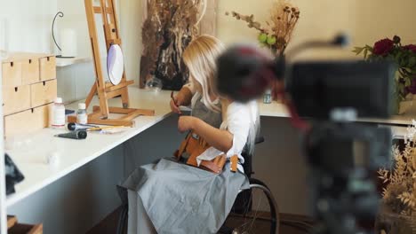 una linda chica rubia en silla de ruedas dibuja y filma a sí misma en video
