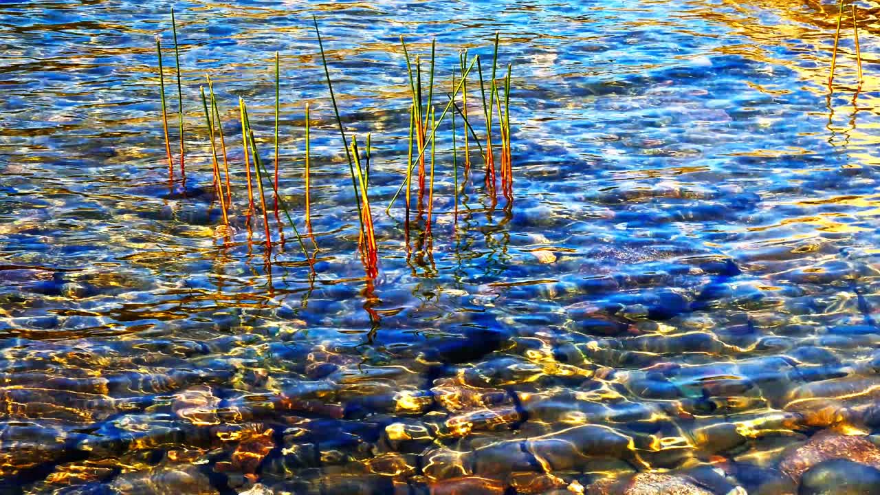 Bright sunlight shines on water in Jordan Pond, Acadia flowing over smooth rocks. The colors of the water and stones create a lively atmosphere