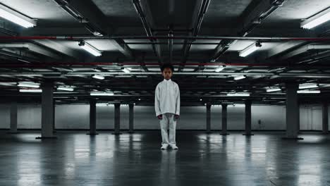 young boy standing alone in the center of a deserted parking garage, dressed in white clothes, surrounded by industrial lights and pipes, evoking feelings of solitude and vulnerability