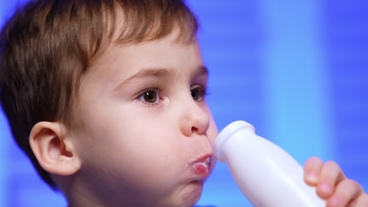 Face of a dark-haired Caucasian toddler boy drinking yogurt from the bottle. Close up portrait of a baby having a snack with dairy.