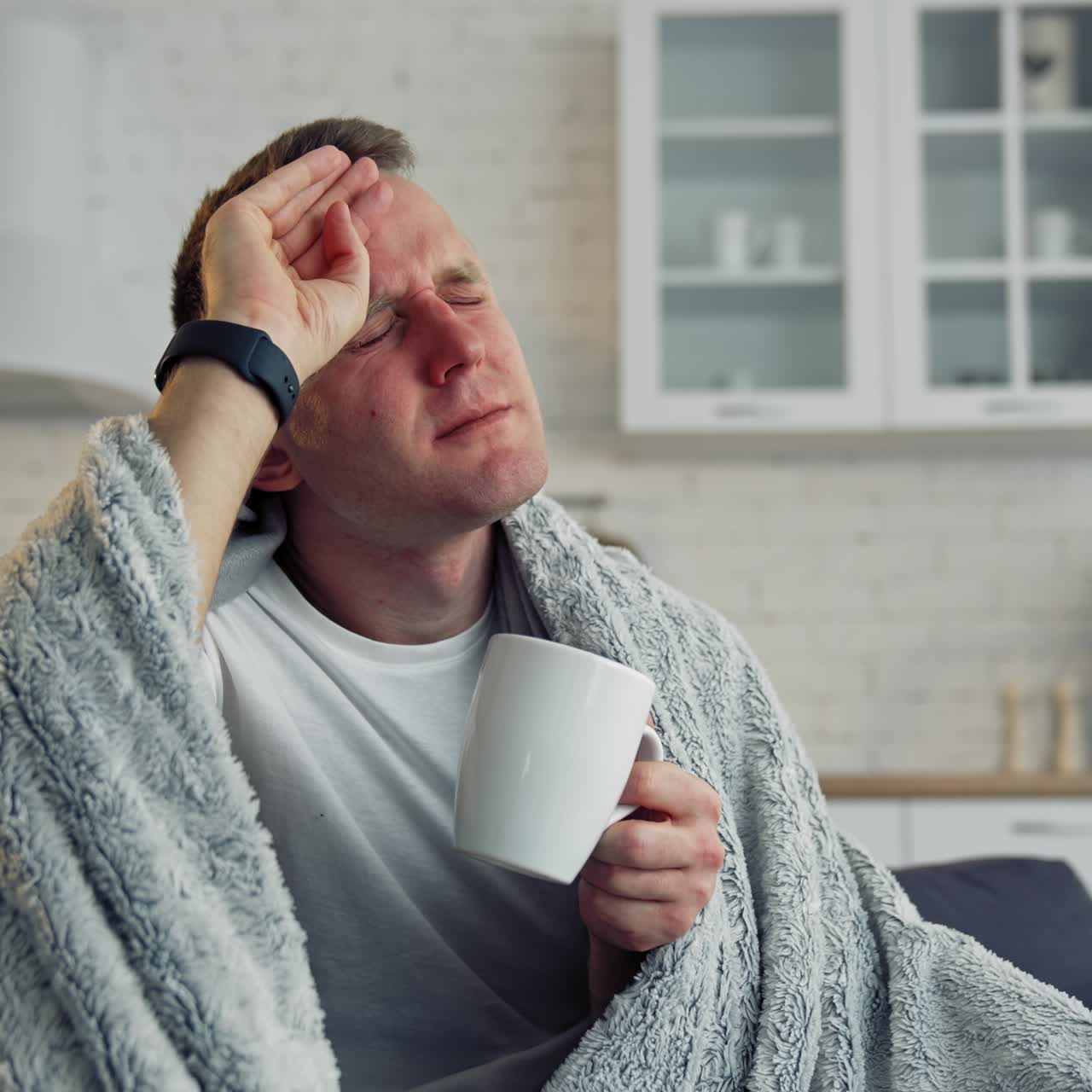 Folk medicine. Sick young man with fever wrapped in warm blanket drinking hot tea. Pandemic