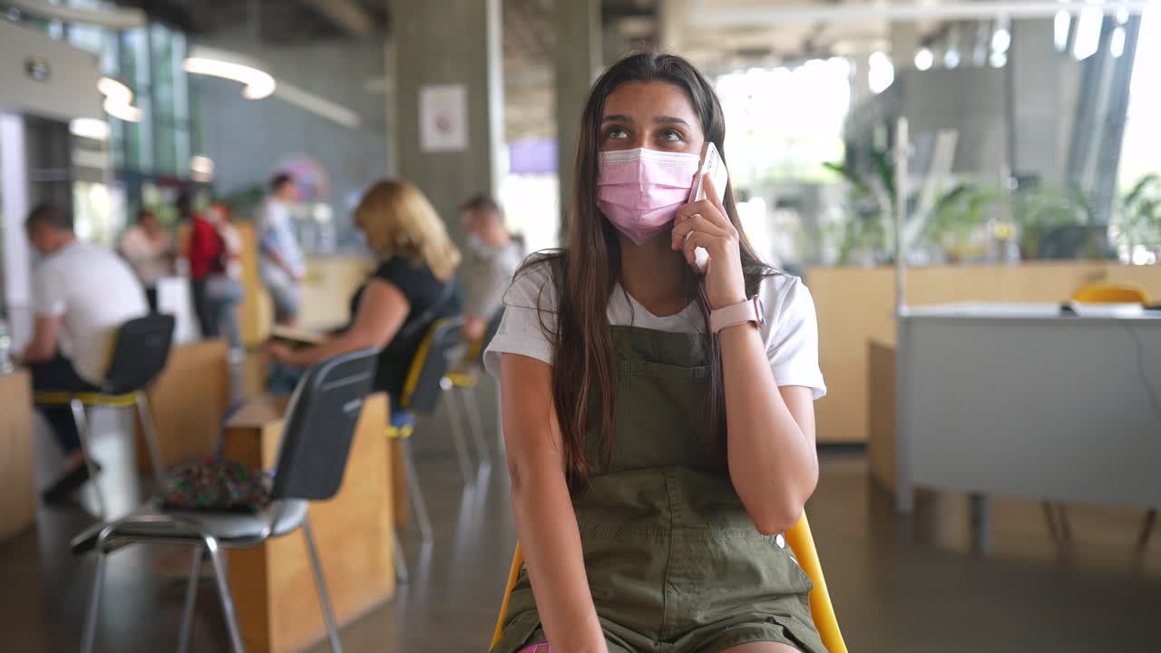 마스크를 착용하고 전화로 대화하는 십대 청소년이 의료실에서 기다리고 있습니다.