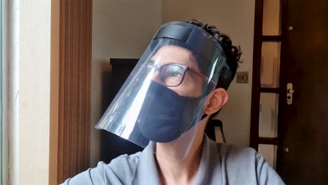 latin young man wearing covid-19 mask and face shield mask is sitting and slowly moving his head to the side