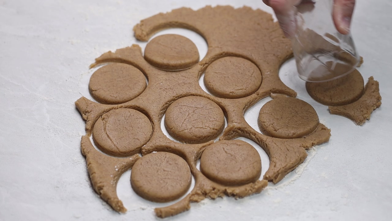 Top down close up of hand cutting cookie dough into round shapes using glass as cutter