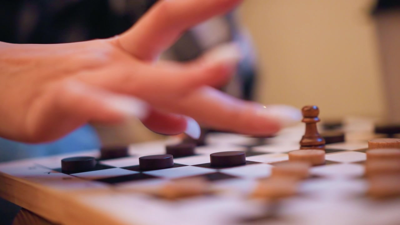 Primo piano di una mano che muove pezzi degli scacchi scuri su una scacchiera con pedoni di legno in primo piano. La scena mostra un posizionamento deliberato dei pezzi, enfatizzando l'interazione tattile tra le dita e il gioco.