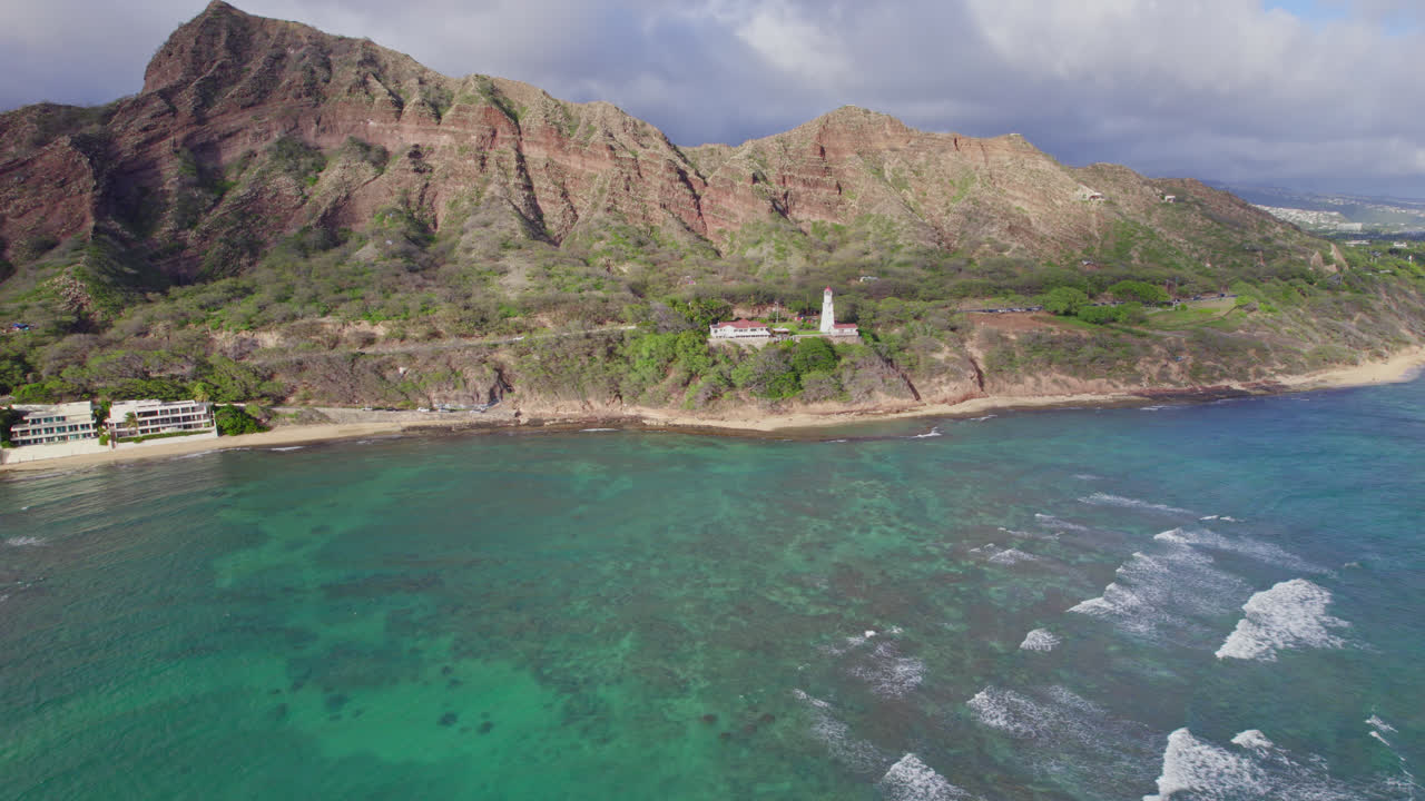 Vista aerea del Faro di Diamond Head con il monte Diamond Head e cielo nuvoloso, con acqua cristallina turchese che si infrange sulla riva