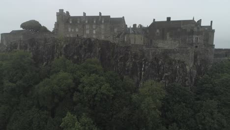 Close-aerial-pan-from-left-to-right-of-Stirling-castle-on-a-overcast-day,-showing-battlements-and-tree-surrounds