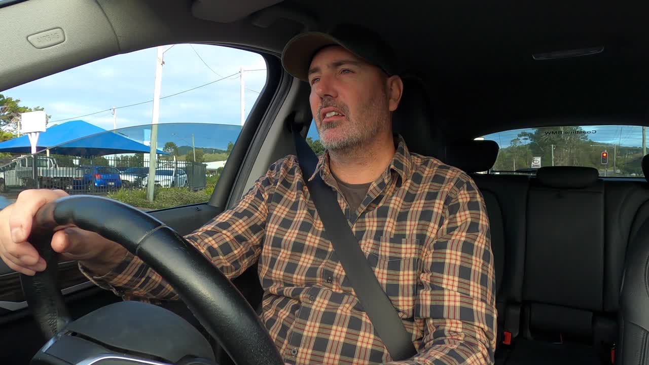 모자를 쓴 남자가 시골 마을에서 태양을 향해 운전하는 동안 눈을 가늘게 뜨고 선바이저를 사용합니다.