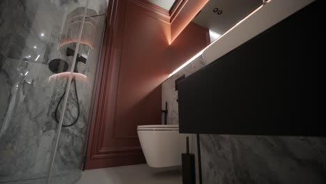 a low-angle view of a luxurious bathroom featuring marble walls, a glass-enclosed shower, terracotta-colored cabinets, and modern fixtures, combining opulence with contemporary design