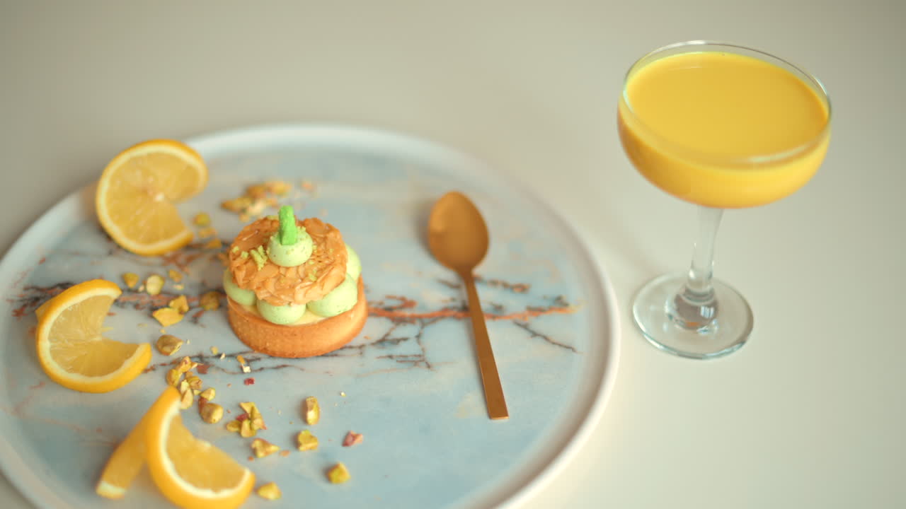 Primer plano de un postre de pistacho con rodajas de limón en un plato cerca de un vaso de zumo de naranja