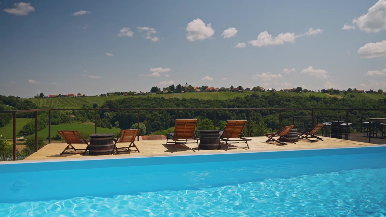 Fredfyldt infinity-pool med træliggestole, klart blåt vand og fantastiske grønne bakker i sollys. Fredfyldt udendørsscene, bredt landskabsudsigt.