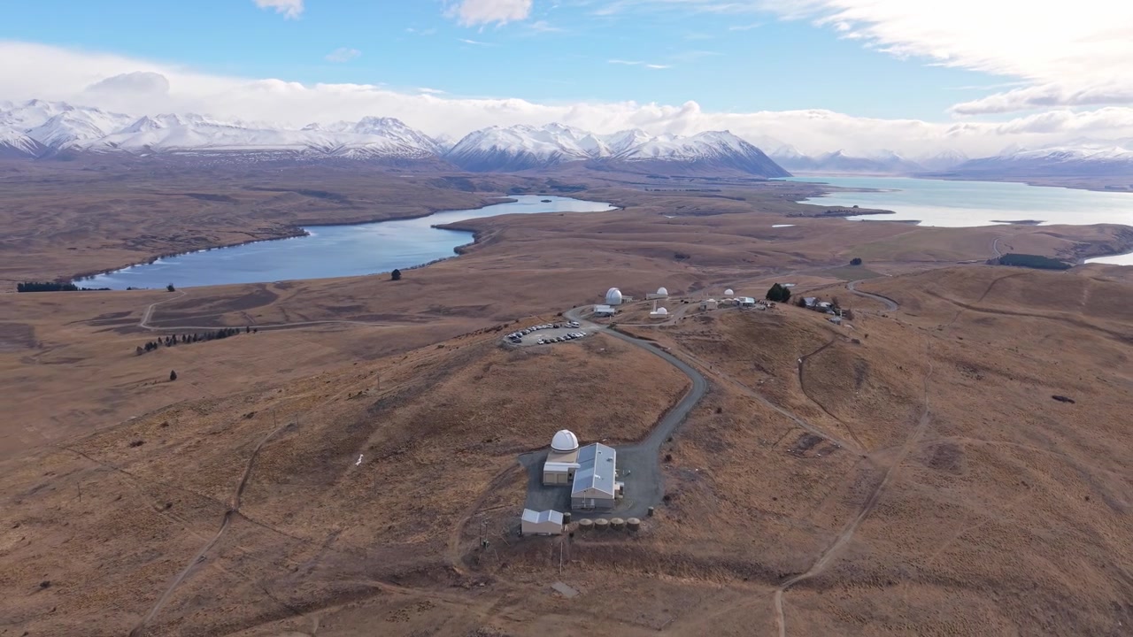 Drone stiger op og trækker sig tilbage over Mount John Observatoriet, hvilket afslører søerne Tekapo og Alexandrina, barskt tørt terræn, omkringliggende bjerge og uberørte gletsjervande