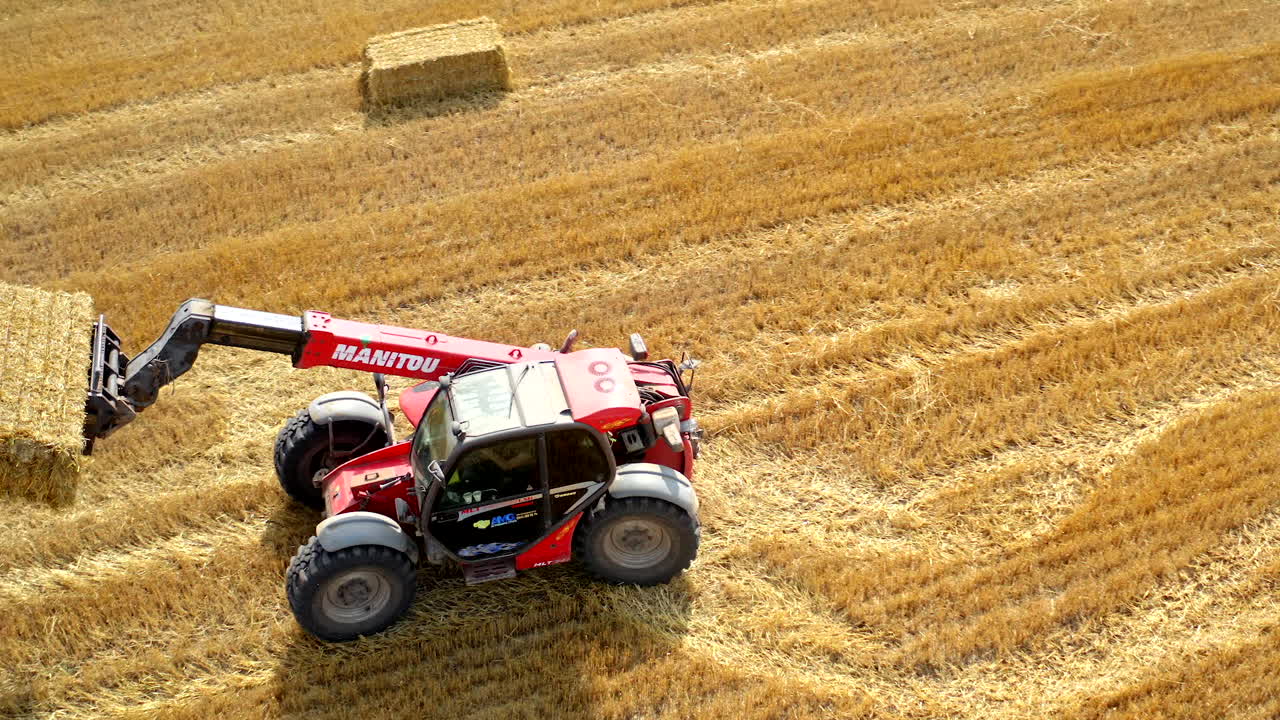 Tractor collecting bales of hay. Aerial view of tractor colecting on agricultural field