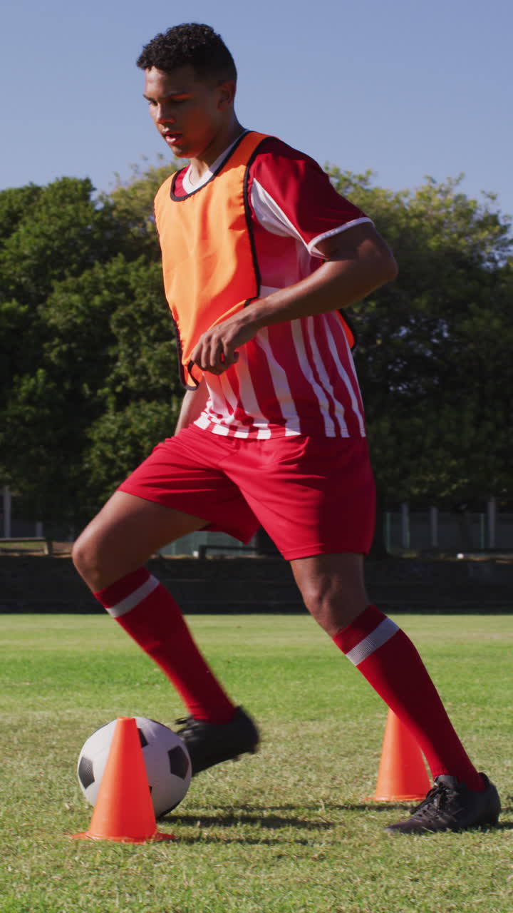 video vertical de un jugador de fútbol biracial en el campo pateando la pelota