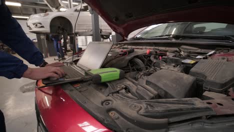 computer diagnostics of cars, young mechanic specialist male uses laptop technology while repairing vehicle with open hood at service station