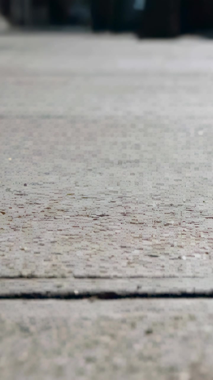 Vertical video: Recording ground camera jittering focus over concrete seam and grit on sidewalk