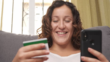 happy young woman shopping with her credit card and cell phone on the couch at home